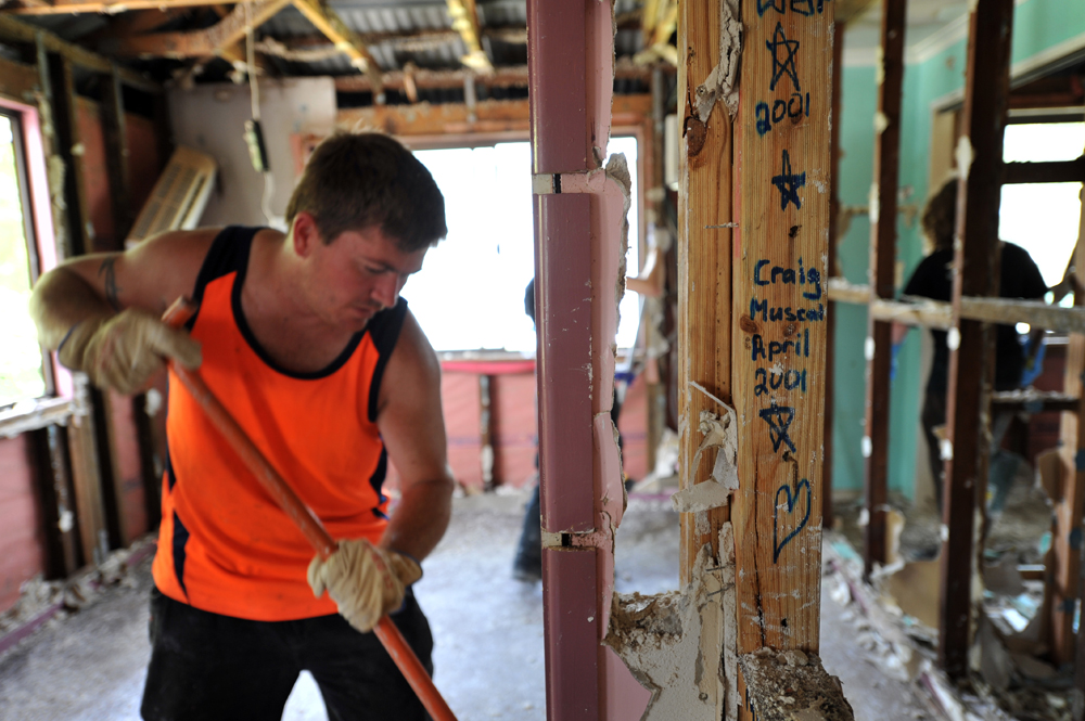 Global Care Volunteer Reg Potter of Oak Flats, sweeps debris around the framework of a house in North Booval, Queensland.