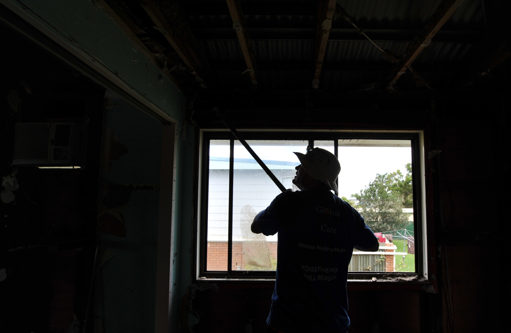 Global Care Volunteer Reg Potter uses a shovel to bring down loose gyprock in a house in North Booval, Queensland.