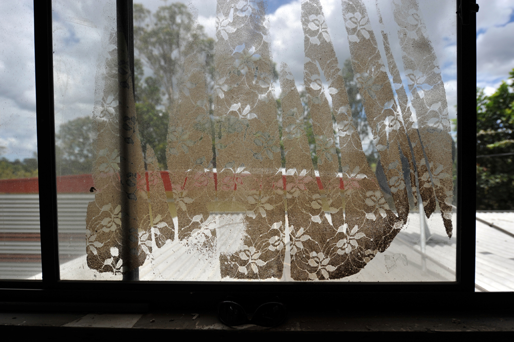 The pattern of a lace curtain is printed onto a glass window as mud residue dries in a house in North Booval, Queensland.